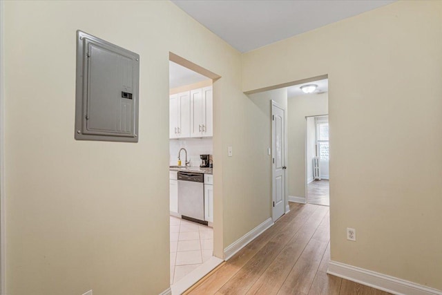 corridor featuring baseboards, a sink, light wood-style flooring, and electric panel