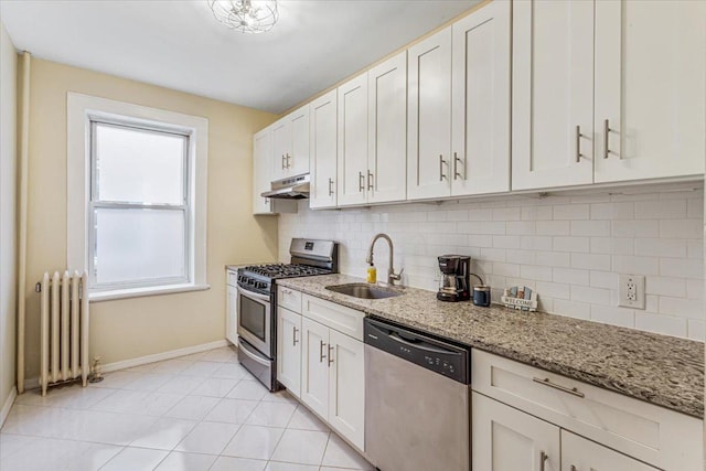 kitchen with a sink, radiator, stainless steel appliances, baseboards, and decorative backsplash