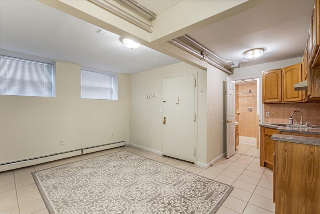 kitchen featuring brown cabinetry, dark countertops, a sink, light tile patterned floors, and a baseboard radiator