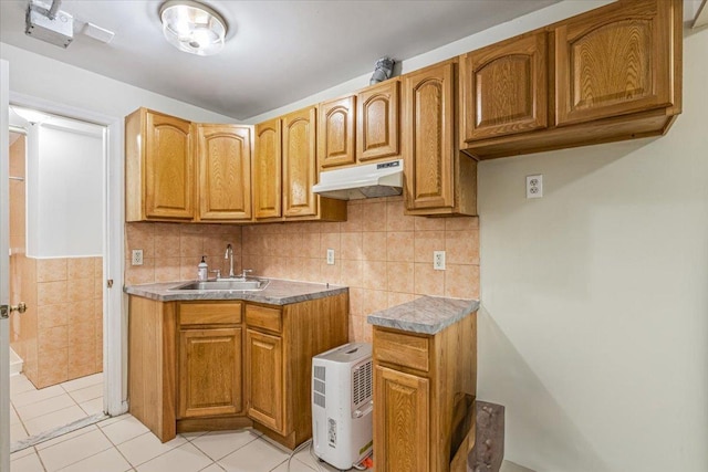 kitchen featuring brown cabinets, light tile patterned flooring, a sink, tasteful backsplash, and under cabinet range hood