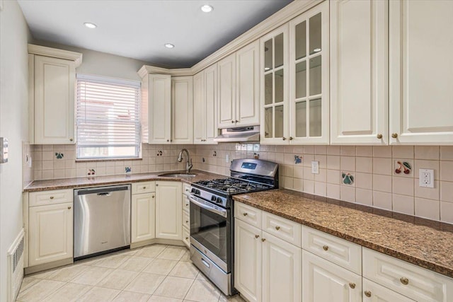 kitchen with under cabinet range hood, appliances with stainless steel finishes, decorative backsplash, and a sink