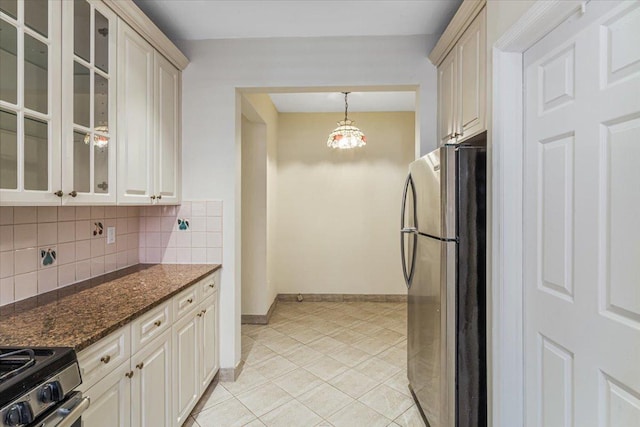 kitchen with freestanding refrigerator, decorative backsplash, glass insert cabinets, baseboards, and a chandelier