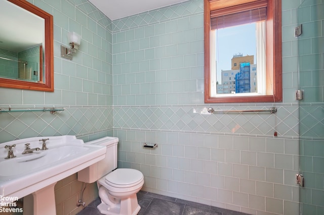 bathroom with toilet, tile patterned floors, tile walls, and a sink