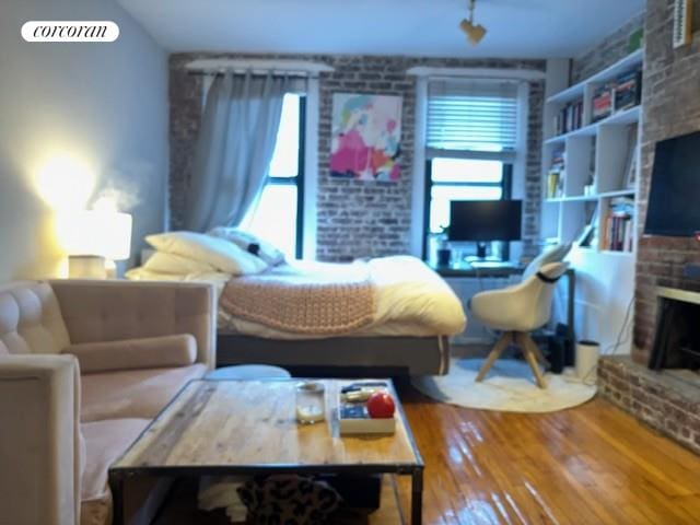 bedroom with a brick fireplace, brick wall, and wood-type flooring