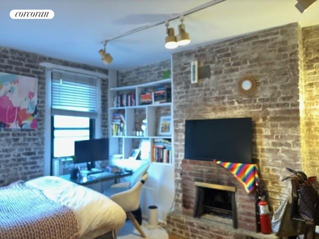 bedroom featuring rail lighting, brick wall, and a fireplace