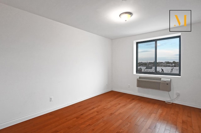 unfurnished room with wood-type flooring, baseboards, and a wall mounted air conditioner