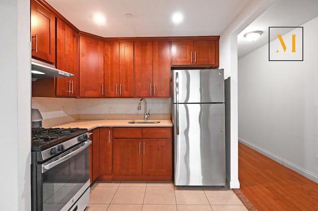 kitchen with a sink, light countertops, stainless steel appliances, baseboards, and under cabinet range hood