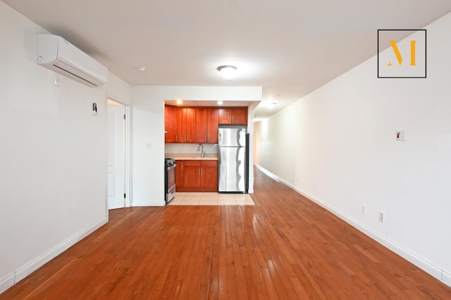 kitchen featuring range with gas cooktop, a wall unit AC, light countertops, freestanding refrigerator, and light wood-style floors