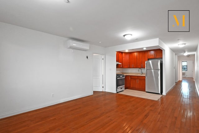 kitchen featuring a sink, light wood-style flooring, freestanding refrigerator, gas range oven, and a wall mounted AC