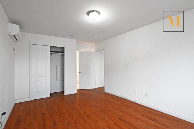 unfurnished bedroom with baseboards, a wall mounted AC, and wood finished floors