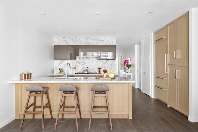 kitchen featuring decorative backsplash, a sink, a peninsula, dark wood-style floors, and a breakfast bar