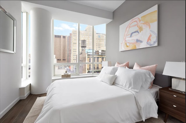bedroom with a view of city, baseboards, multiple windows, and wood finished floors