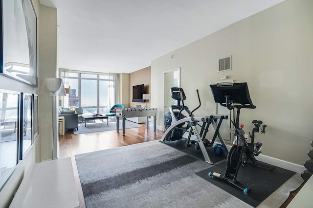 workout room featuring visible vents, baseboards, wood finished floors, and a wall of windows