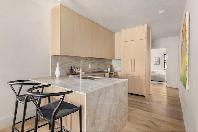 kitchen featuring a peninsula, light brown cabinetry, light stone countertops, modern cabinets, and a sink