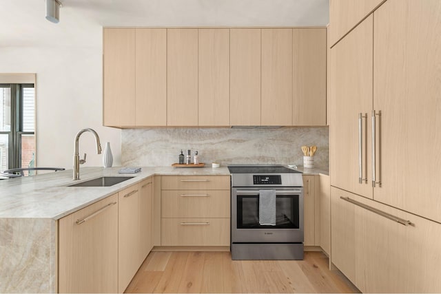 kitchen featuring light brown cabinetry, modern cabinets, stainless steel range with electric cooktop, a sink, and a peninsula