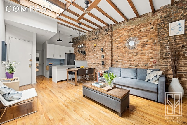 living room featuring a ceiling fan, brick wall, a towering ceiling, beam ceiling, and light wood-style flooring