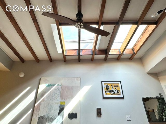 interior space featuring a ceiling fan, beamed ceiling, and a skylight