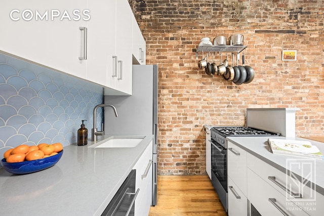 kitchen with dishwashing machine, gas range, light countertops, white cabinetry, and a sink