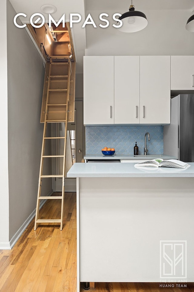 kitchen featuring light countertops, light wood-style flooring, freestanding refrigerator, white cabinetry, and tasteful backsplash