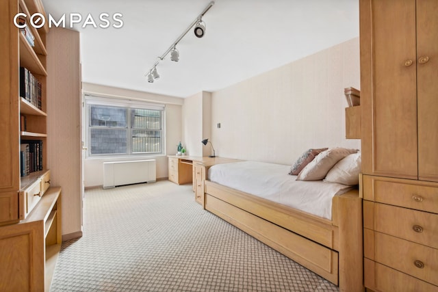 bedroom with radiator heating unit, baseboards, rail lighting, and light colored carpet
