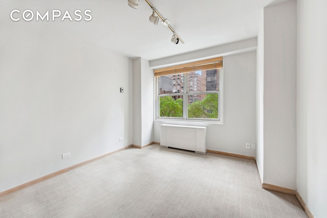 spare room with track lighting, baseboards, and radiator heating unit