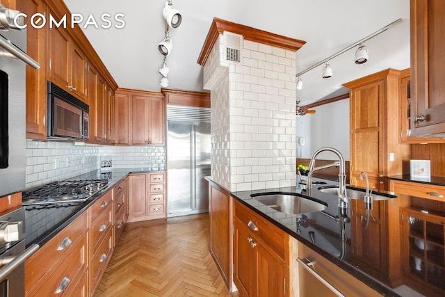 kitchen featuring track lighting, brown cabinetry, dark stone countertops, and appliances with stainless steel finishes