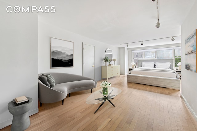 bedroom with wood-type flooring, rail lighting, and baseboards