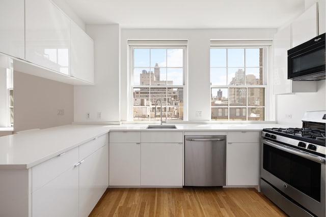 kitchen with a healthy amount of sunlight, appliances with stainless steel finishes, white cabinets, and light wood-style flooring