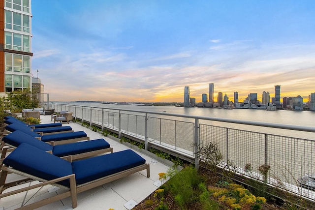 patio terrace at dusk featuring an outdoor living space, a water view, and a balcony