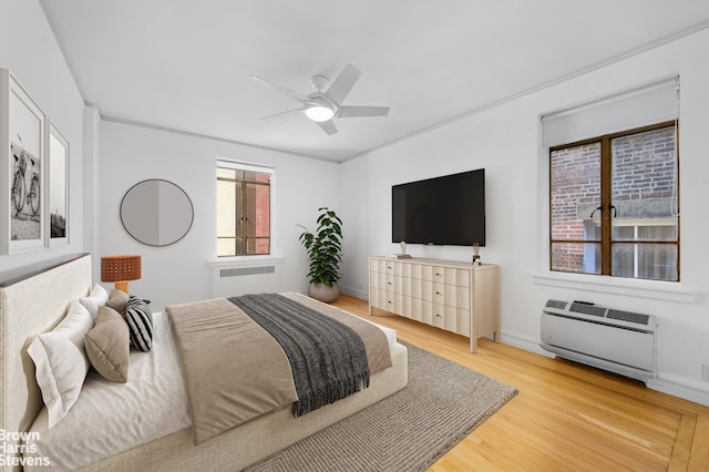 bedroom with a ceiling fan, light wood-type flooring, baseboards, an AC wall unit, and radiator heating unit