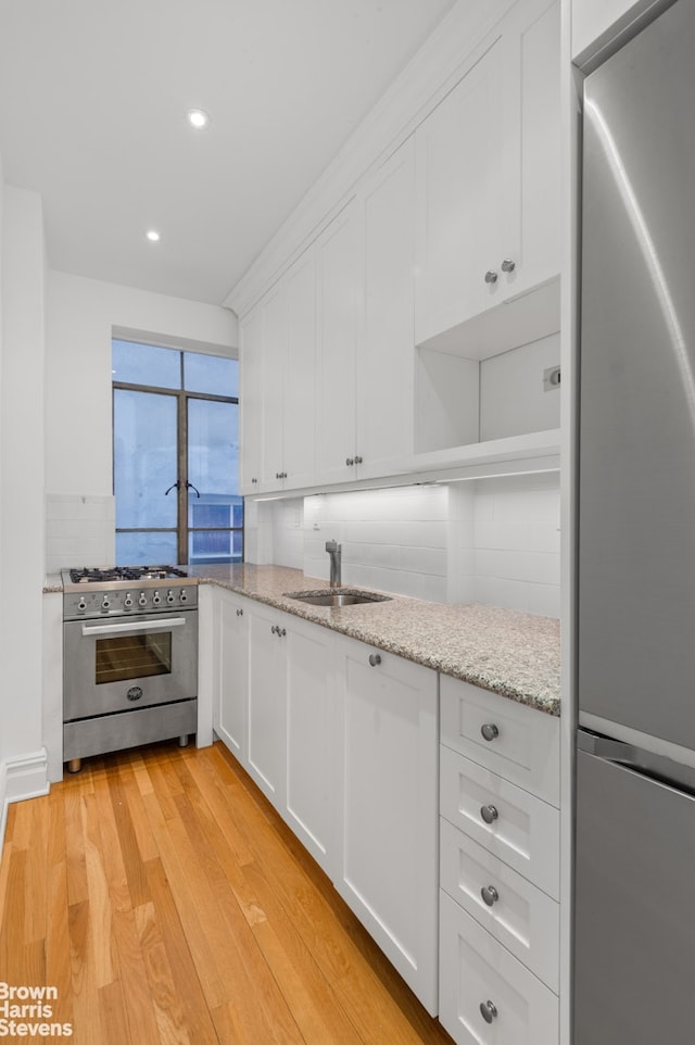 kitchen featuring white cabinets, light stone counters, a sink, light wood finished floors, and appliances with stainless steel finishes