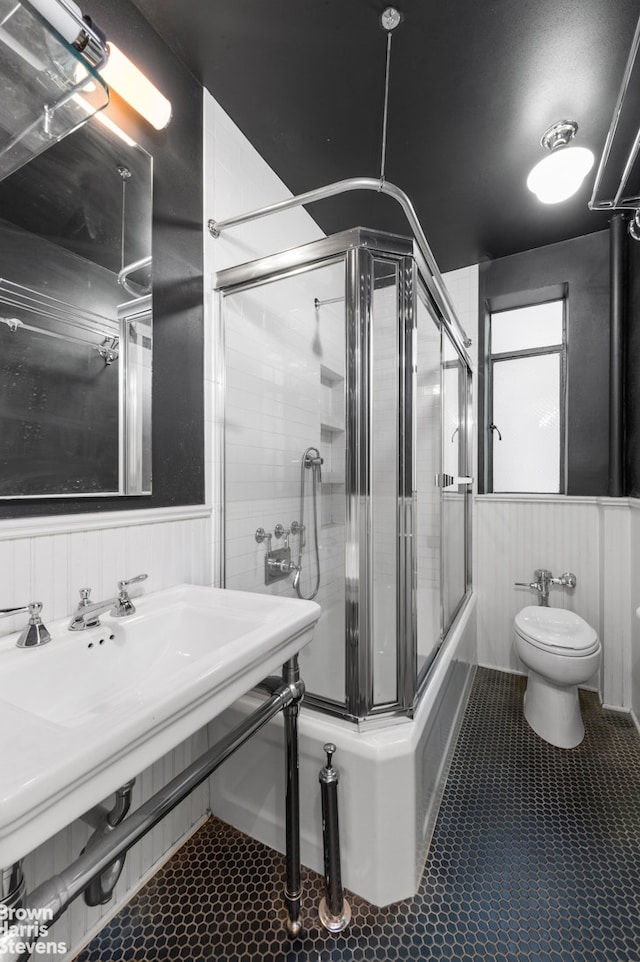 full bathroom featuring tile patterned flooring, wainscoting, toilet, and shower / bath combination with glass door