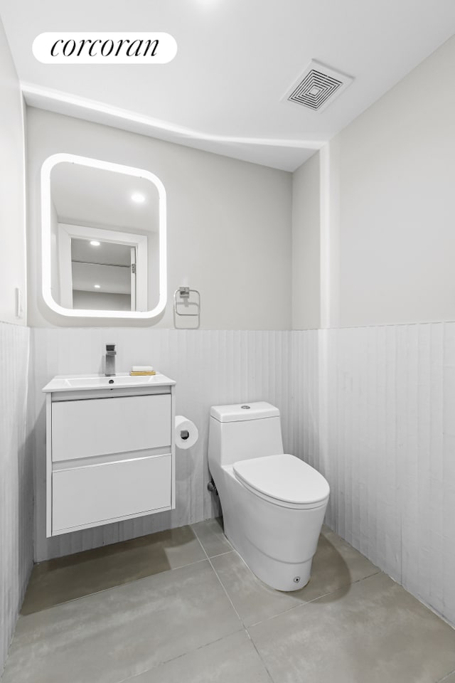 bathroom with finished concrete floors, a wainscoted wall, toilet, and vanity