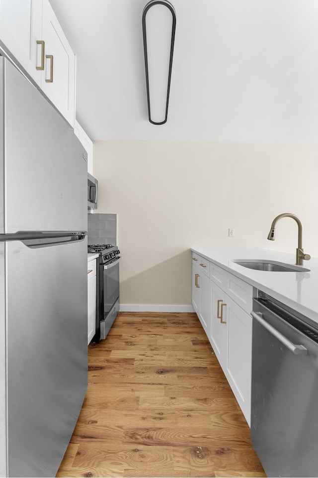 kitchen with a sink, baseboards, light countertops, stainless steel appliances, and white cabinetry