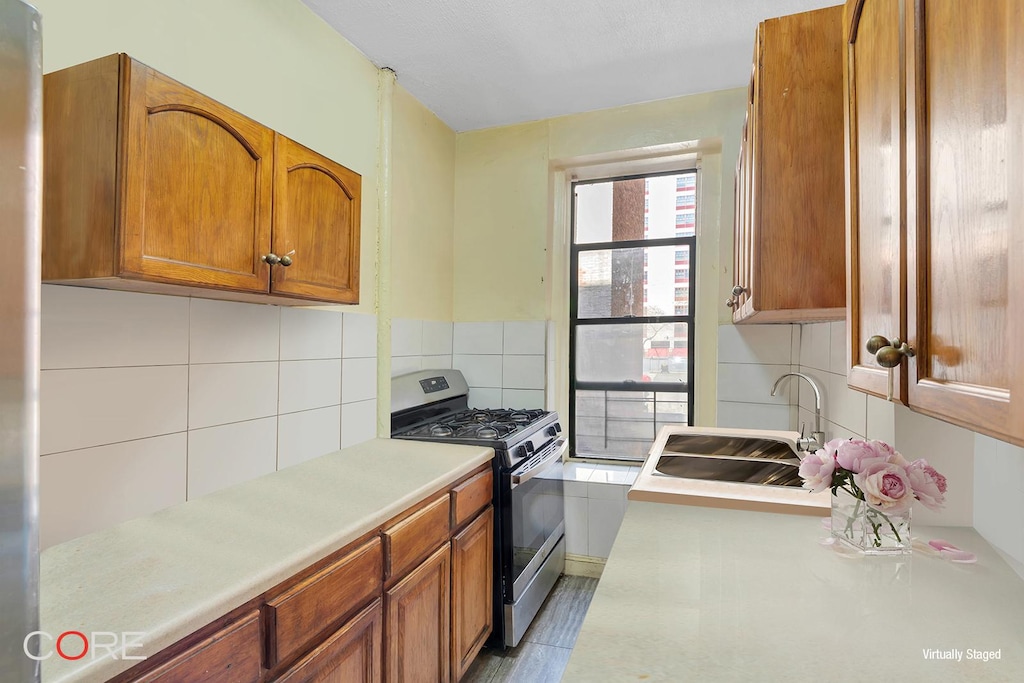 kitchen featuring a sink, stainless steel gas stove, light countertops, brown cabinetry, and backsplash