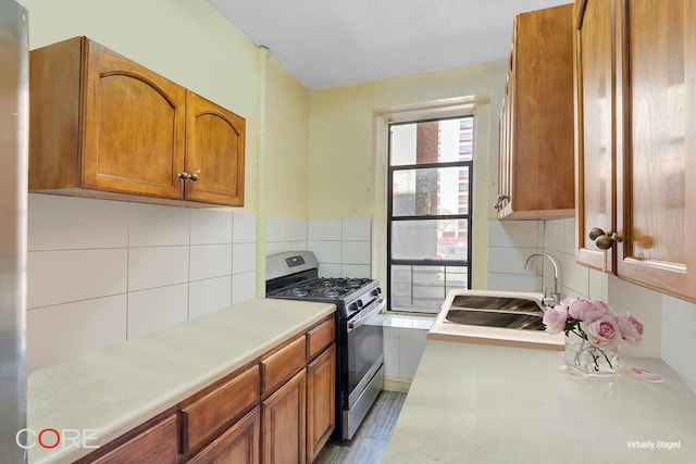 kitchen featuring a sink, stainless steel gas stove, light countertops, brown cabinetry, and backsplash