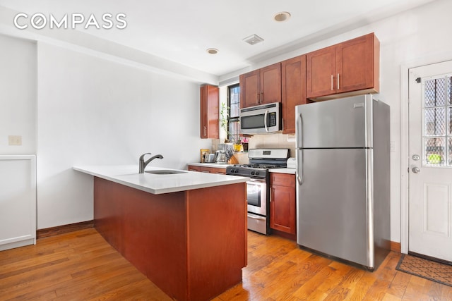 kitchen with a peninsula, light countertops, a sink, light wood-style flooring, and appliances with stainless steel finishes