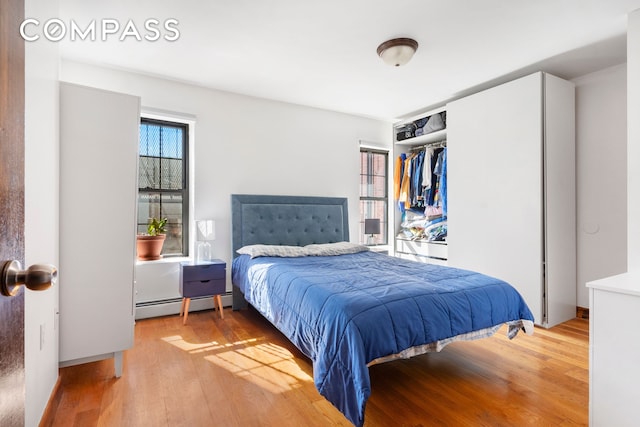 bedroom featuring light wood-type flooring, a baseboard radiator, and a closet