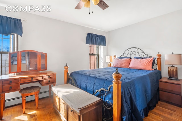 bedroom with ceiling fan, baseboard heating, and wood finished floors