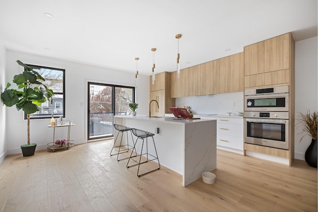 kitchen featuring light wood-style floors, modern cabinets, a kitchen island with sink, and a sink
