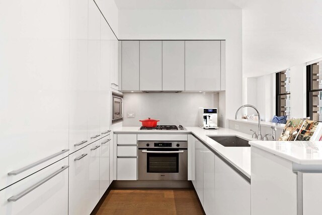 kitchen with appliances with stainless steel finishes, modern cabinets, a sink, white cabinets, and a peninsula