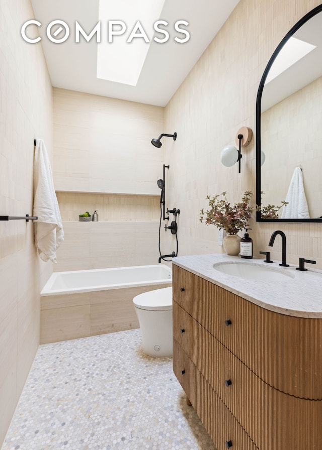 bathroom with vanity, toilet, a skylight, and tile walls