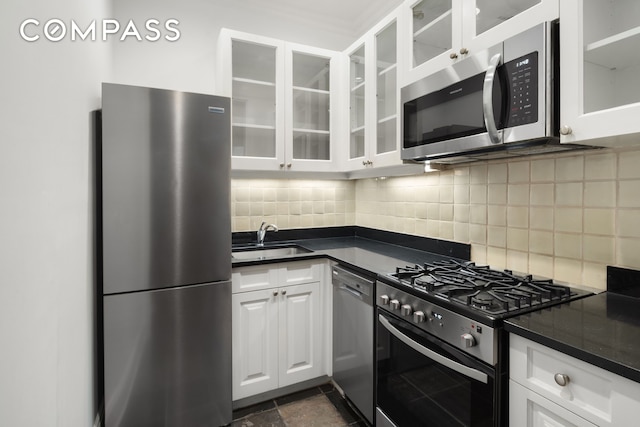 kitchen with a sink, backsplash, dark countertops, and stainless steel appliances