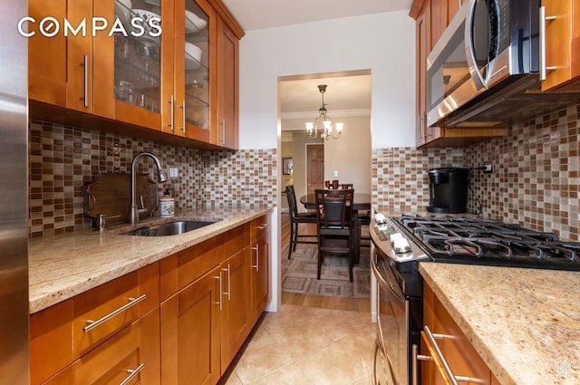 kitchen with appliances with stainless steel finishes, light stone countertops, brown cabinets, a sink, and ornamental molding