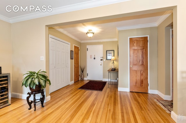 foyer entrance featuring beverage cooler, ornamental molding, light wood finished floors, and baseboards