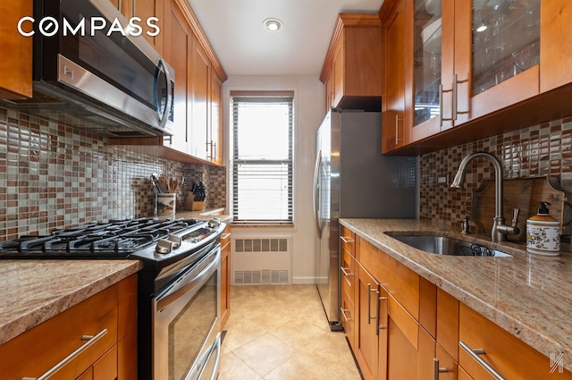 kitchen featuring brown cabinetry, a sink, appliances with stainless steel finishes, and light stone countertops