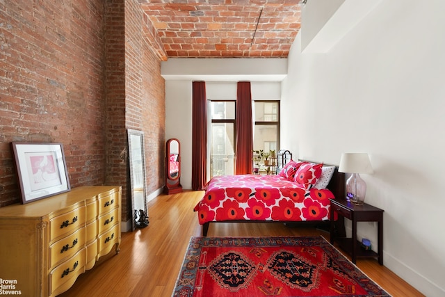 bedroom featuring baseboards, brick ceiling, wood finished floors, and brick wall