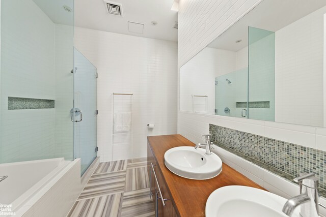 full bathroom with a bath, a stall shower, decorative backsplash, double vanity, and tile walls