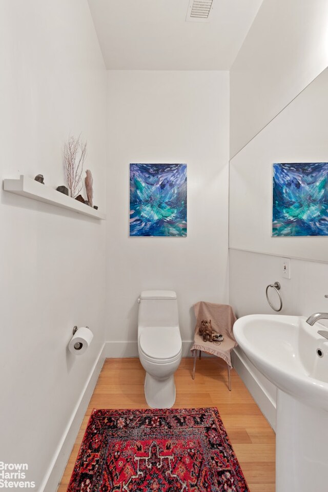 half bathroom featuring wood finished floors, toilet, and baseboards