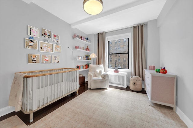 bedroom with a nursery area, baseboards, wood finished floors, and radiator